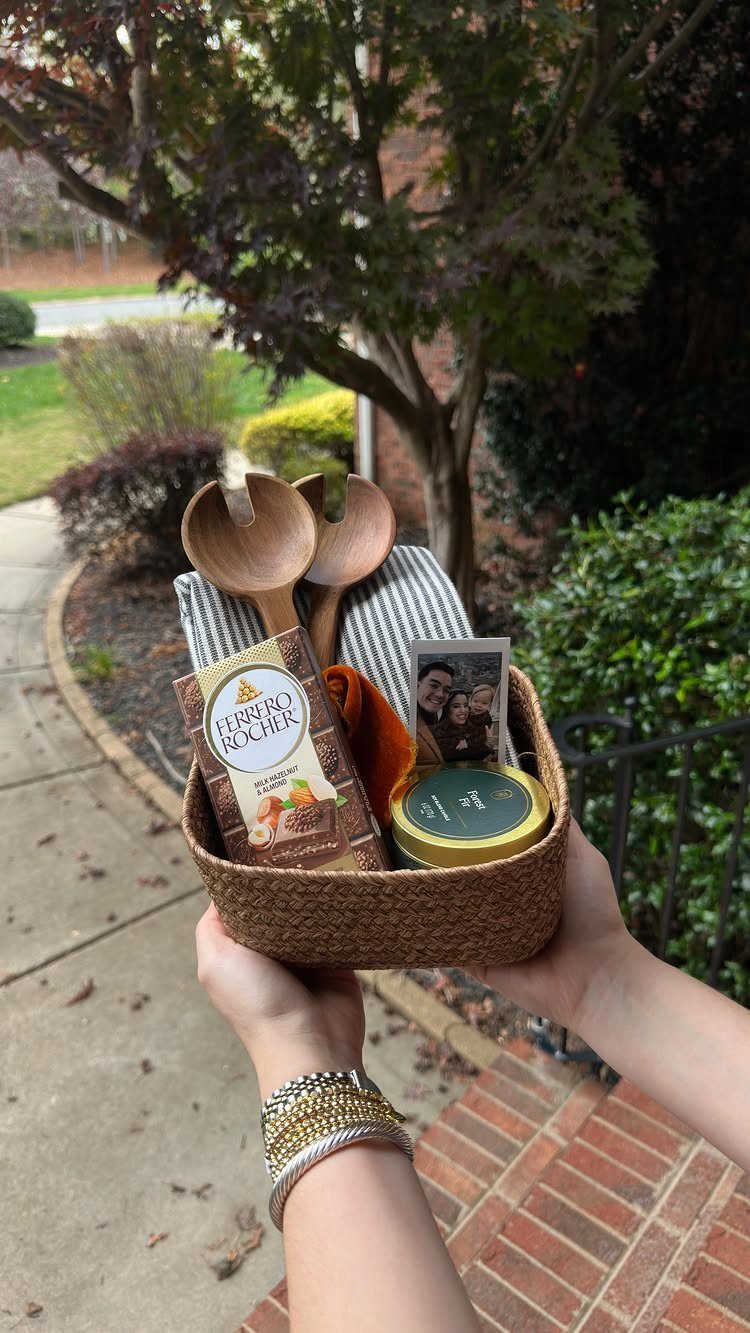 Woven gift basket with chocolates, wooden spoons, and a photo held outdoors.