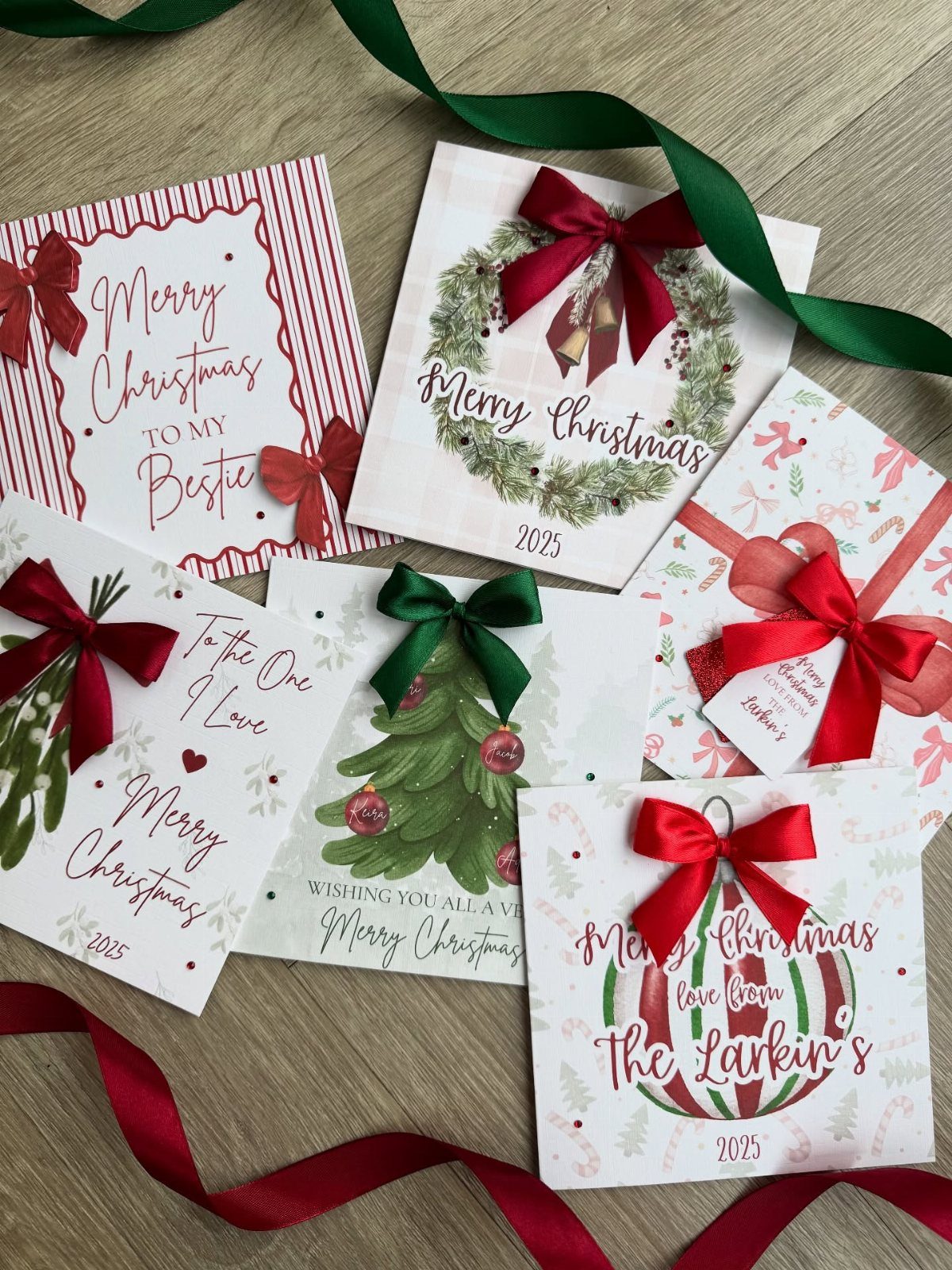 Christmas cards with red bows and holiday illustrations on a wooden surface.
