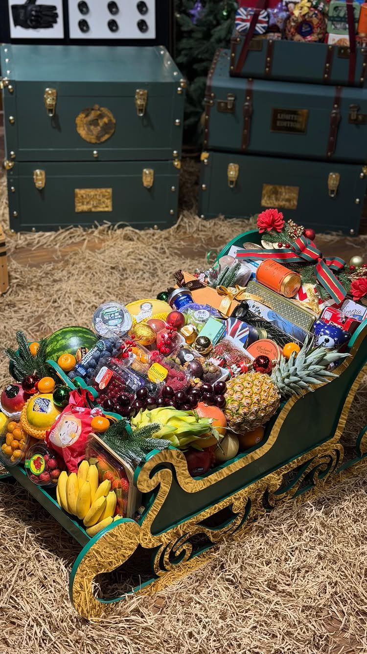 Green decorative sleigh filled with assorted fruits and gift packages on straw background