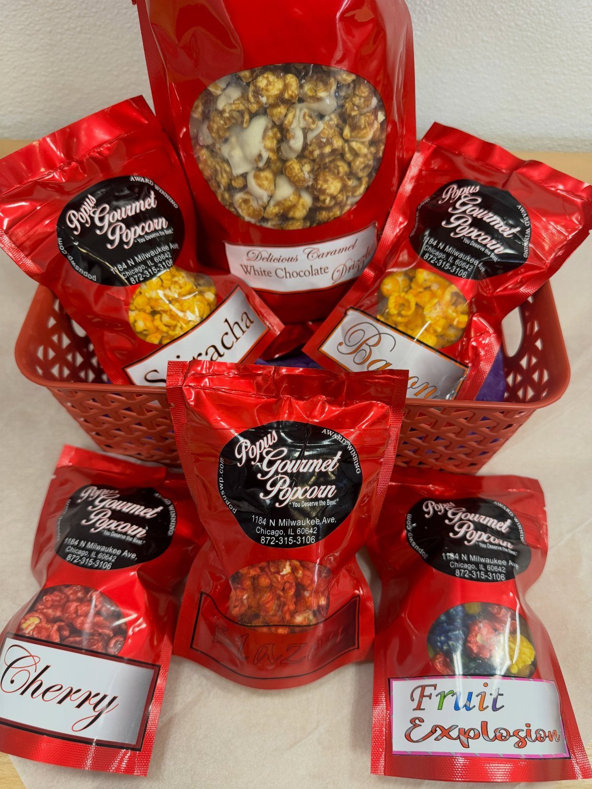 Red foil bags of gourmet popcorn arranged in a brown woven basket.