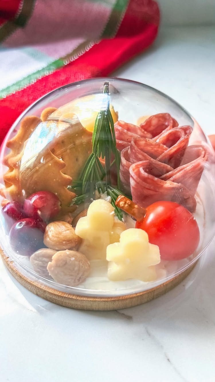 Charcuterie assortment with salami, cheese, and fruit in a clear plastic dome container.
