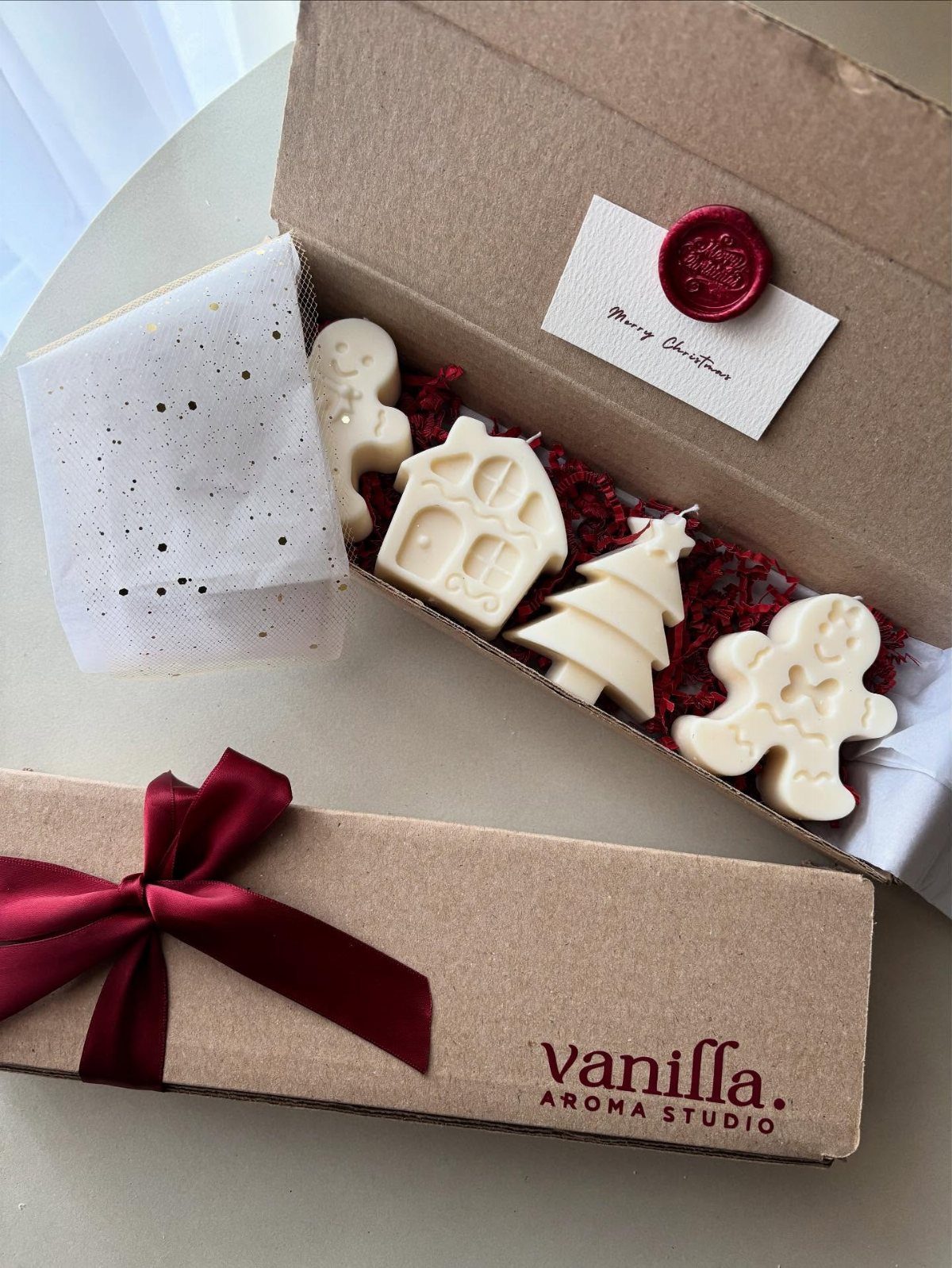 White Christmas shaped candles in a cardboard gift box with a red ribbon.