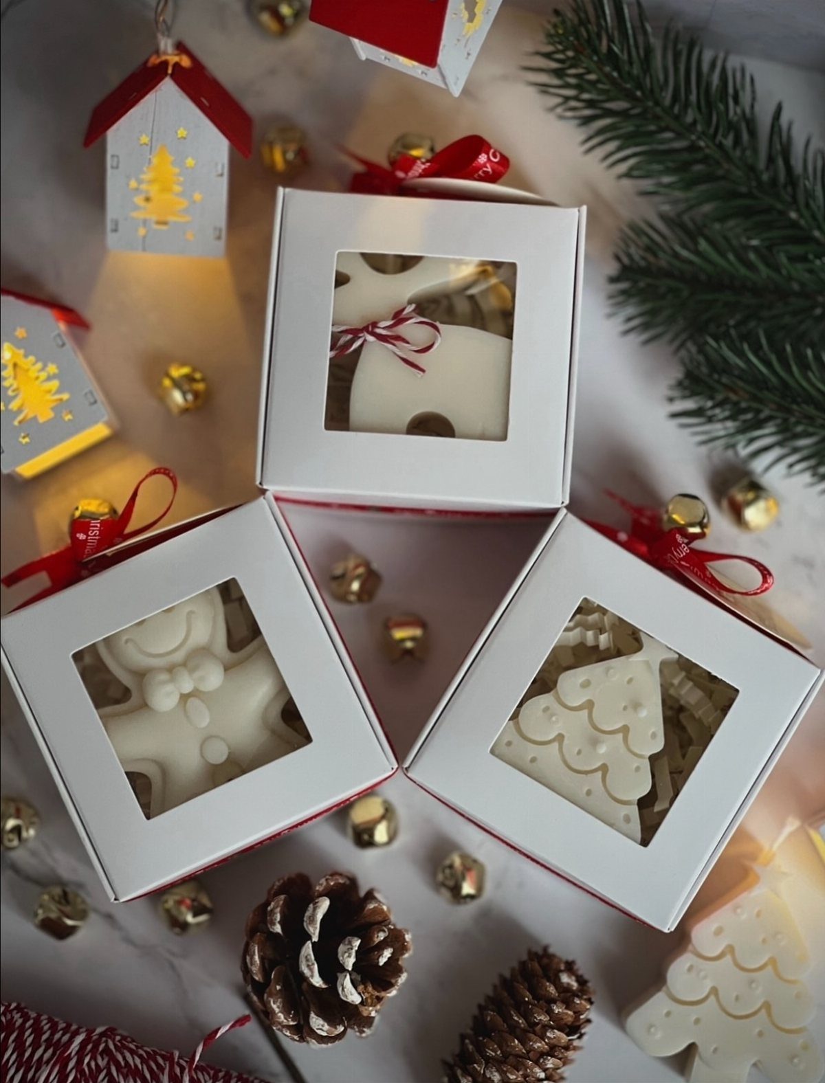 White gift boxes with Christmas treats surrounded by pine cones and gold bells.