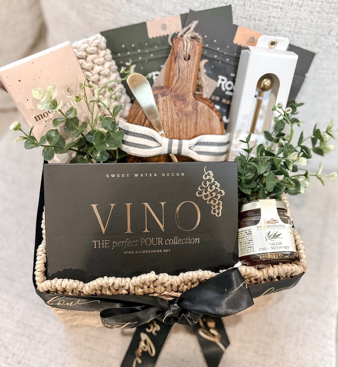 Woven gift basket with wine accessories, a wooden board, and gourmet treats.