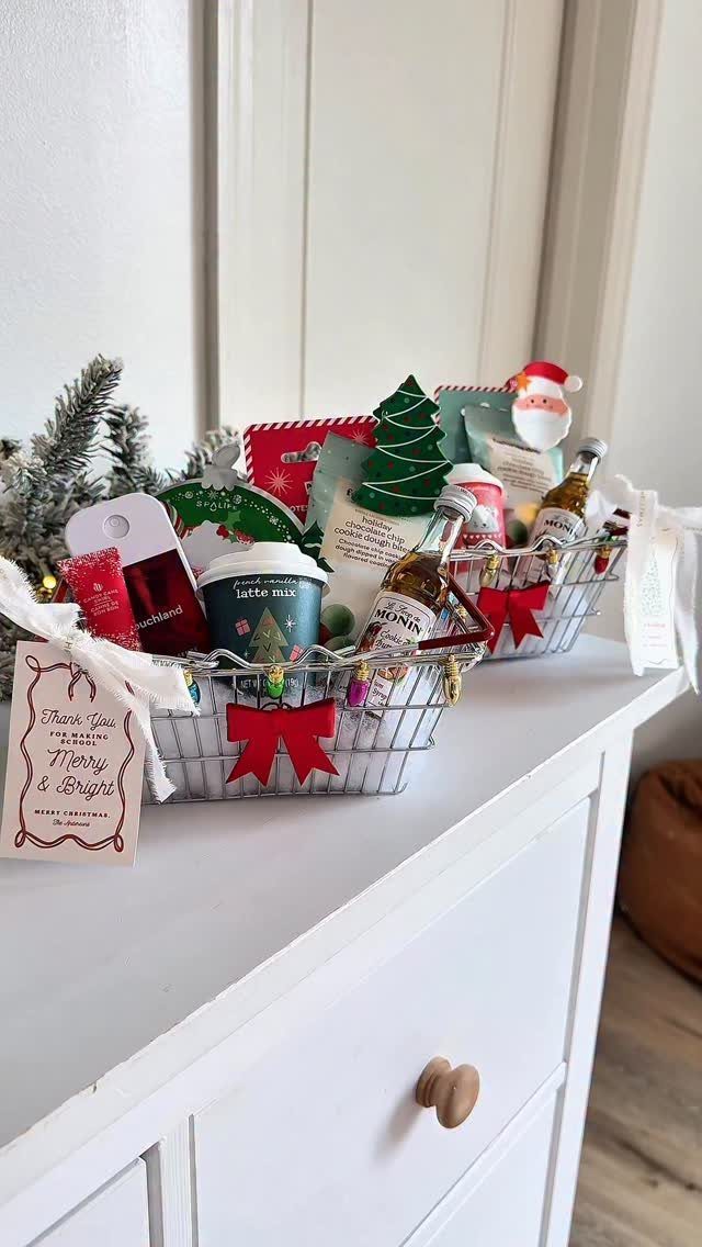 Two wire gift baskets with coffee, mini bottles, and Christmas decorations on a dresser.