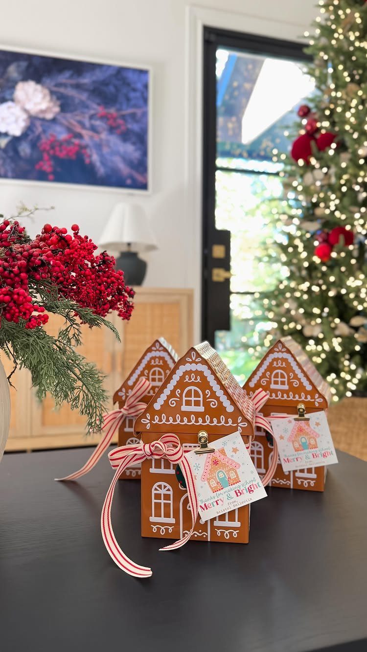 Gingerbread house gift boxes with red striped ribbons on a dark table.