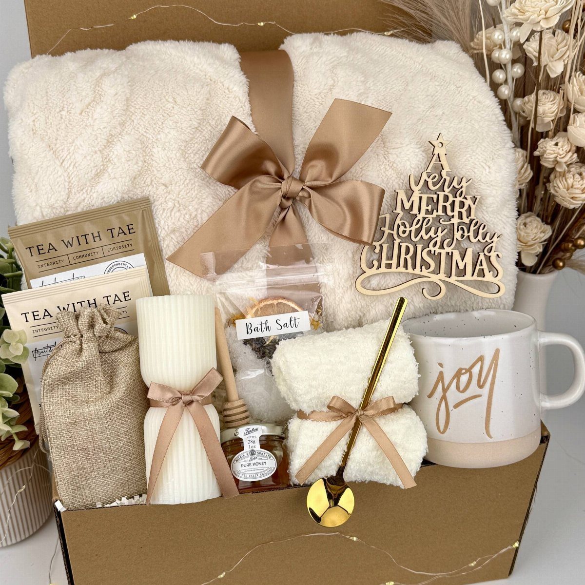 Gift box with white fluffy blanket, tea, candle, and joy mug for Christmas.