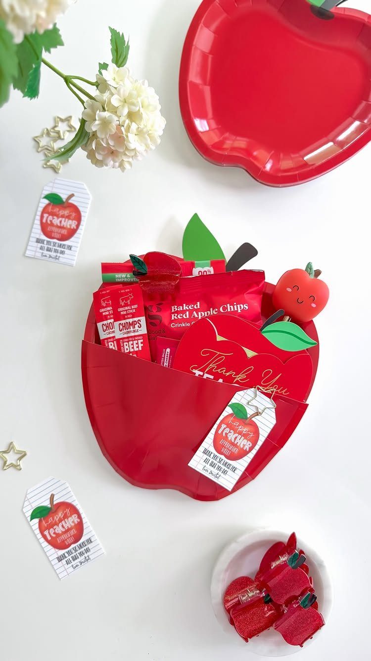 Red apple-shaped gift basket filled with red snacks and apple-themed tags.