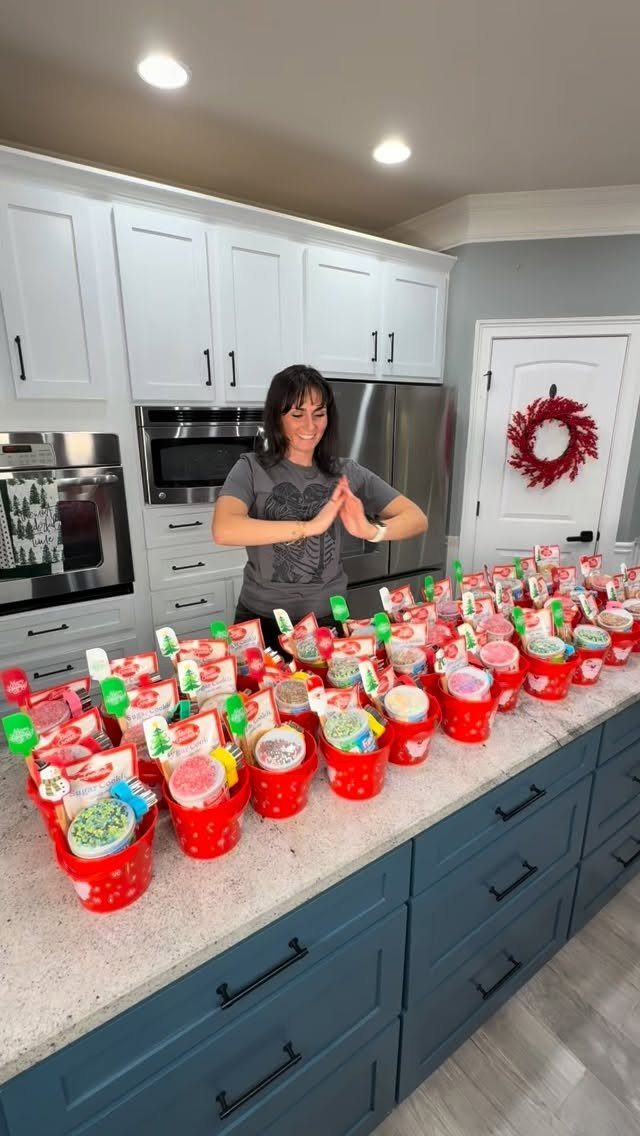 Woman standing behind a kitchen counter filled with many red Christmas gift buckets.