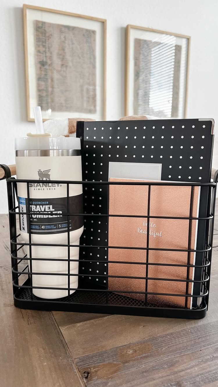 Black wire gift basket with a white tumbler and rose-gold notebook on wood.