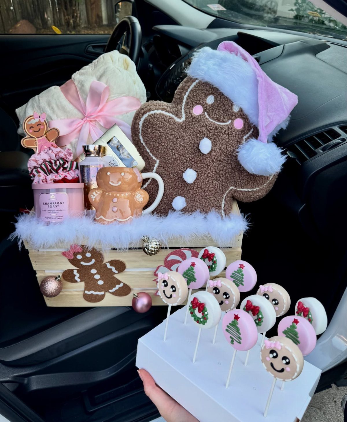 Gingerbread themed gift basket with plush, mug, and decorated cake pops in a car.