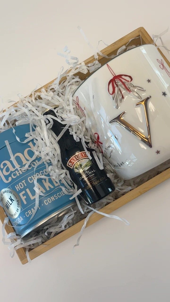 Hot chocolate gift basket with a blue tin, syrup bottle, and white mug.