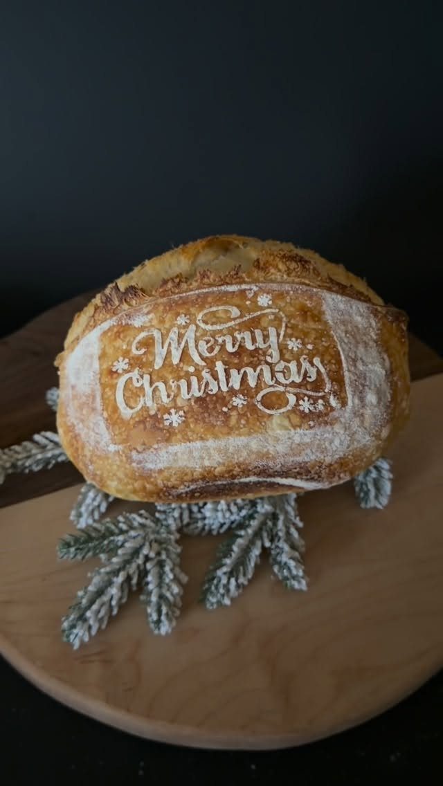 Sourdough bread loaf with Merry Christmas scored into the crust on wooden board