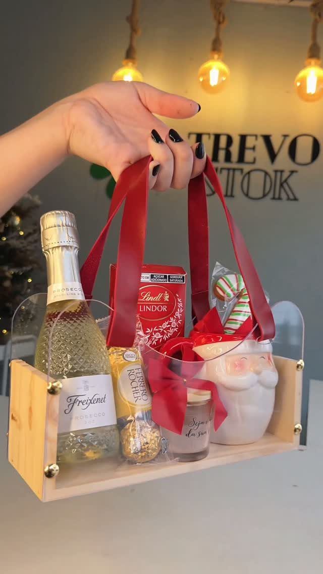 Wooden gift tray with sparkling wine, chocolates, and a Santa mug held by ribbons.
