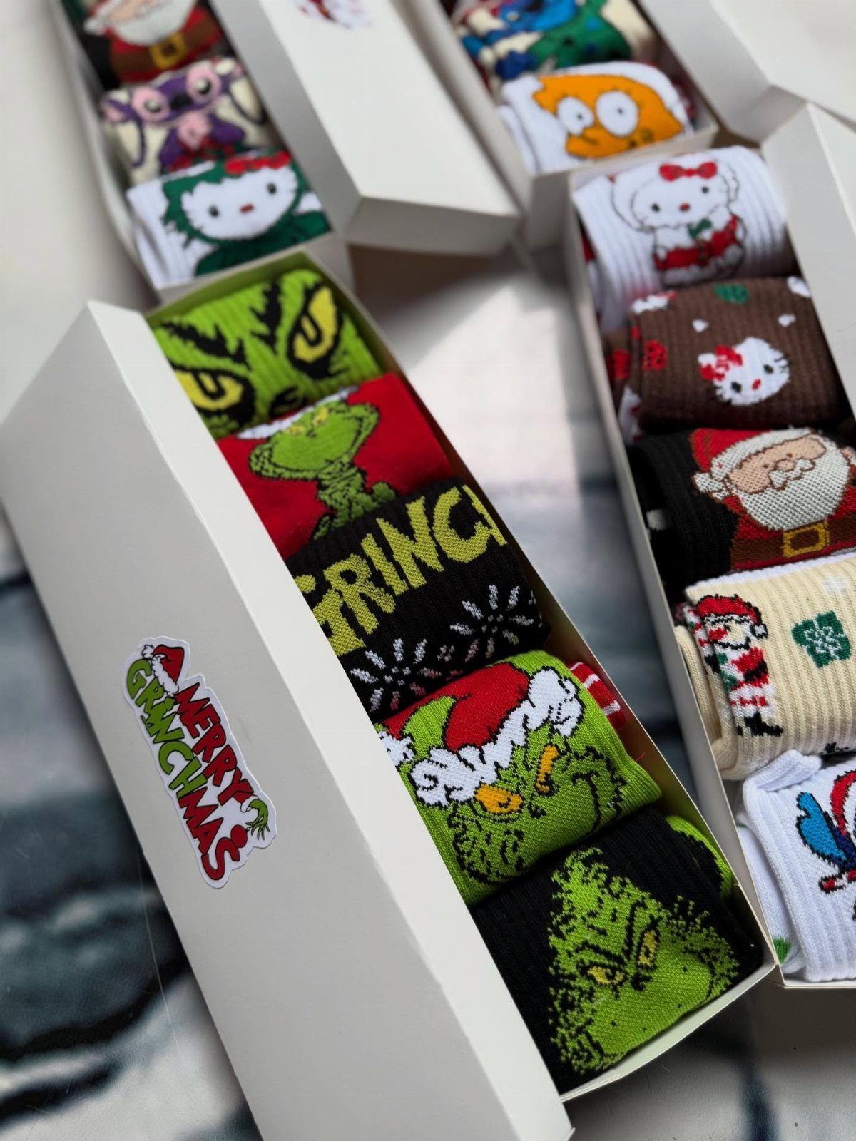 Christmas themed socks with Grinch and Santa designs arranged in white gift boxes.