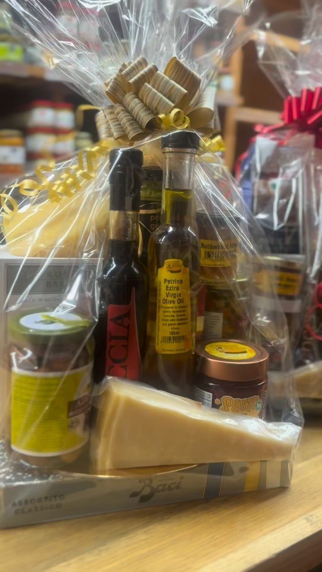 Gourmet gift basket with cheese, oils, and preserves wrapped in clear cellophane.