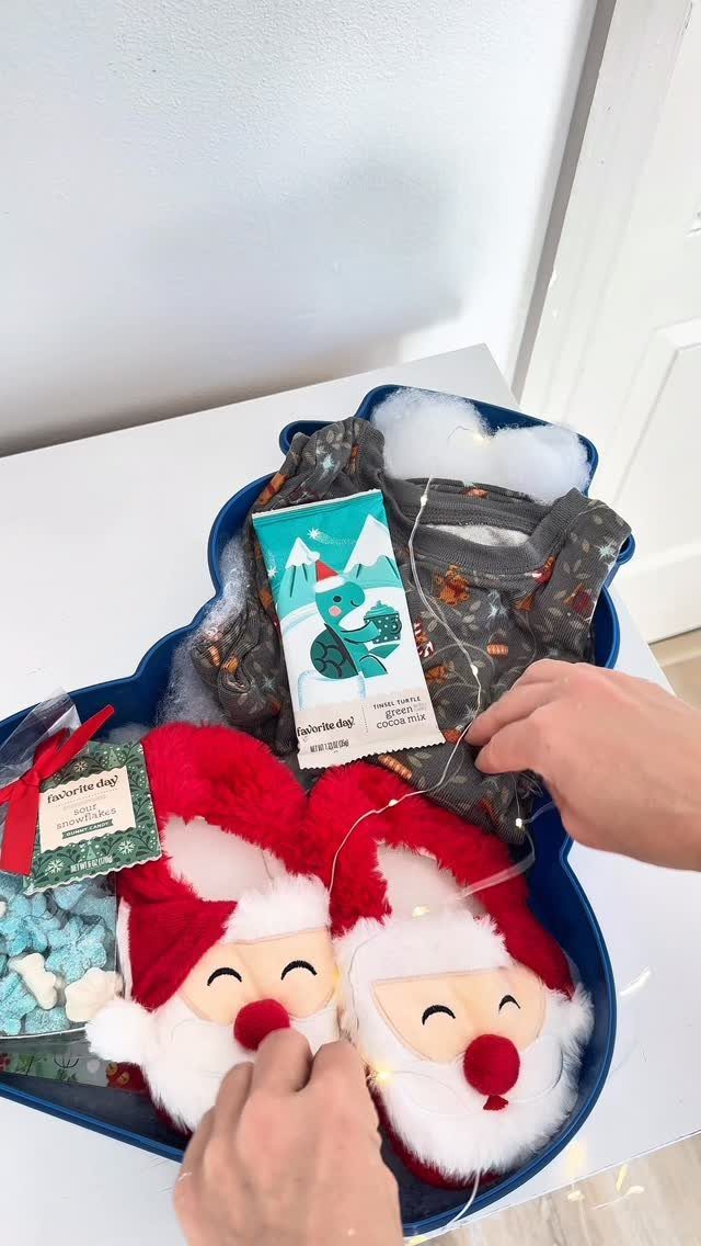 Blue gift tray with Santa slippers, grey clothing, and twinkling fairy lights.