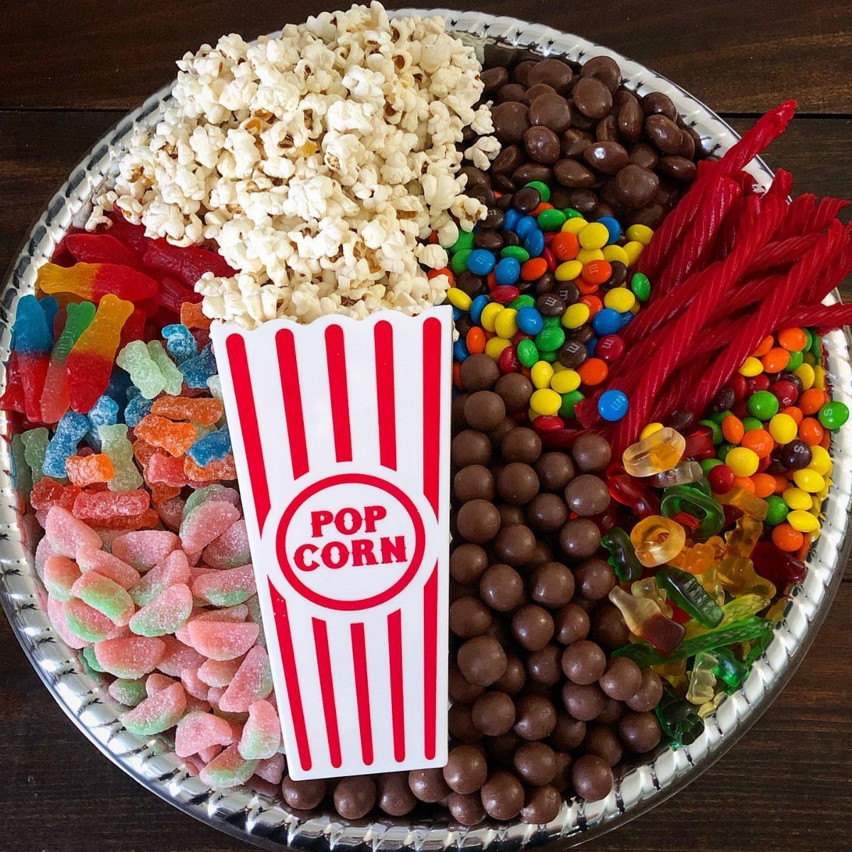 Assorted movie candies and popcorn arranged on a silver serving tray.