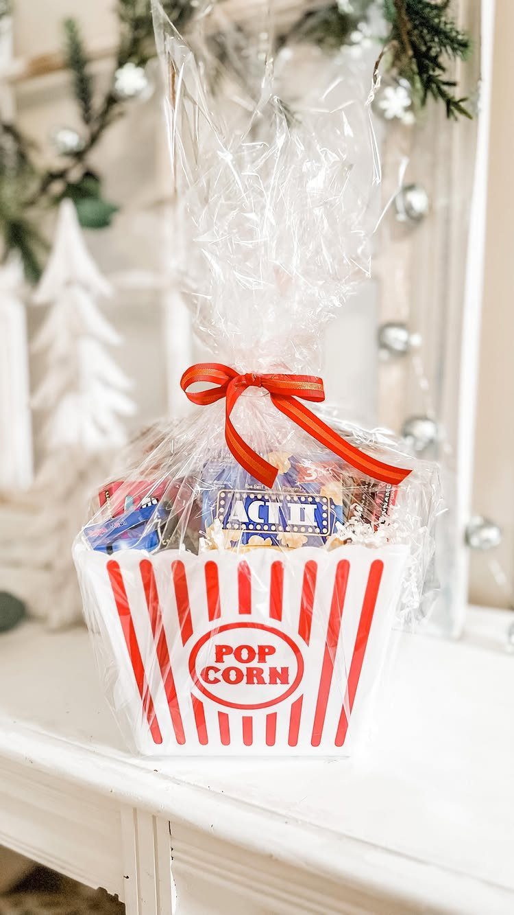 Popcorn bucket gift basket with snacks wrapped in cellophane and a red ribbon.