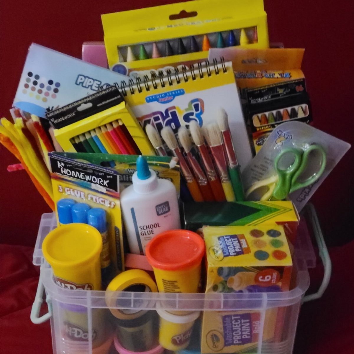 Clear plastic bin filled with colorful art supplies, paintbrushes, and sketching materials.