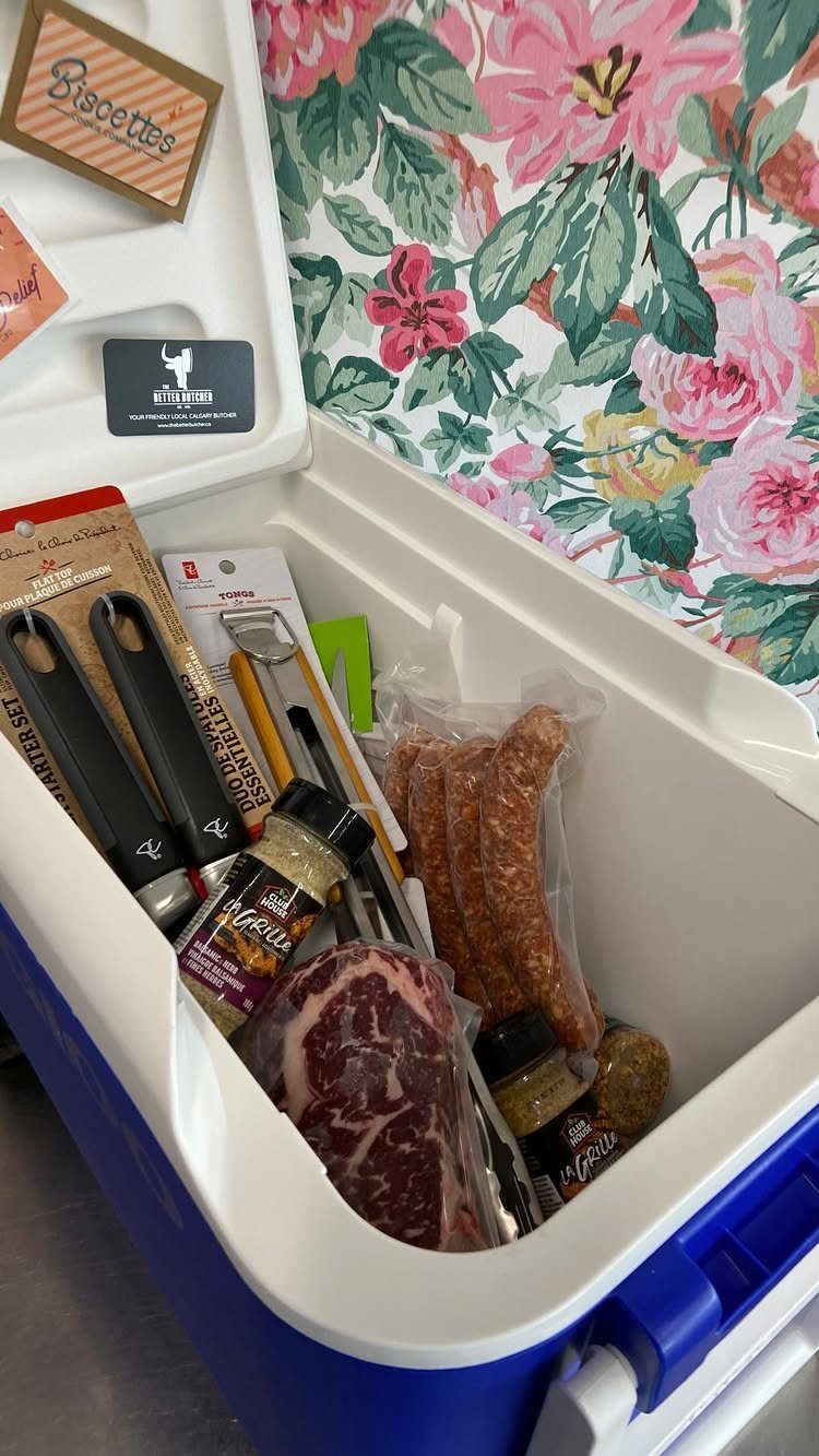 Blue and white cooler filled with steaks, sausages, and kitchen tools for a raffle.