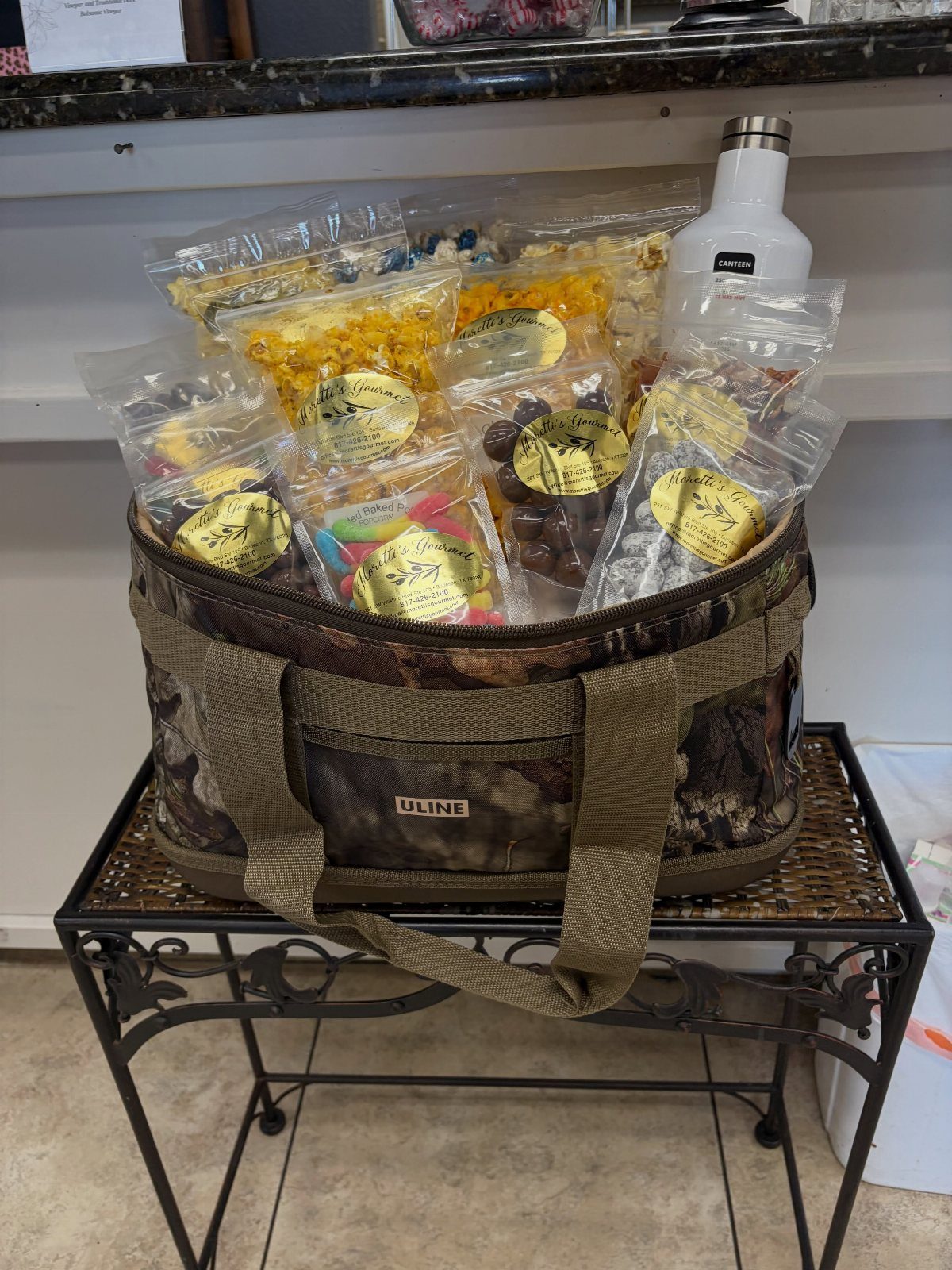 Camouflage cooler bag filled with assorted bagged candies and a white thermos.