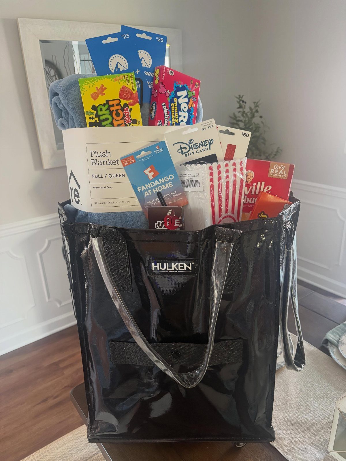 Black glossy bag filled with movie snacks, gift cards, and a blue blanket.