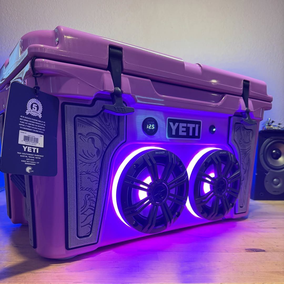 Purple Yeti cooler with integrated speakers and glowing purple LED lights on wood.