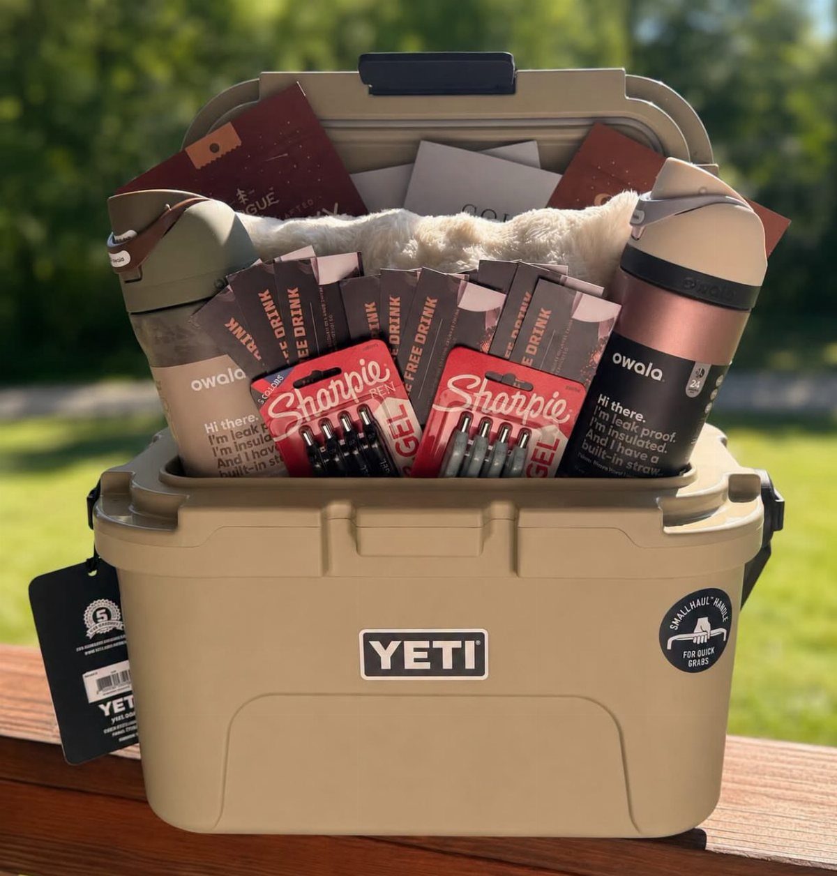 Tan Yeti cooler filled with water bottles, markers, and gift cards on wood.