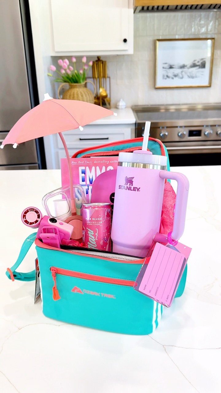 Turquoise cooler bag filled with pink accessories, a purple tumbler, and a pink umbrella.