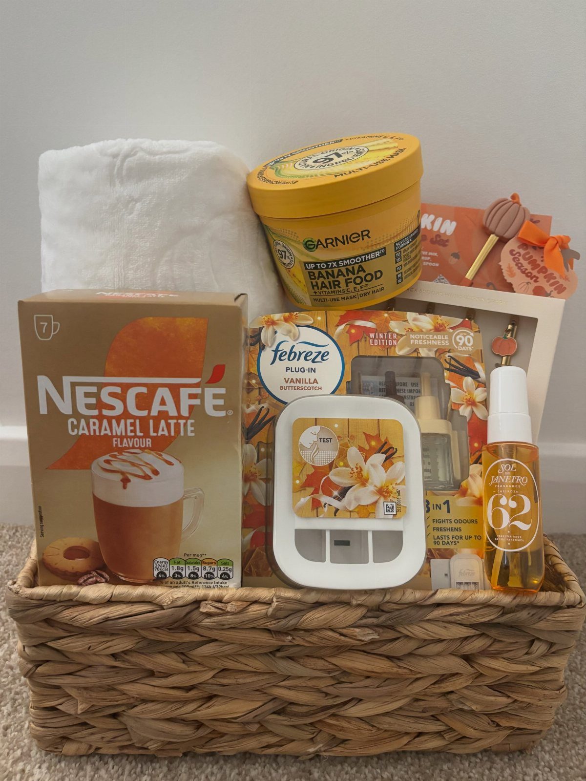 Woven wicker basket containing a white fluffy towel, coffee, and beauty products.