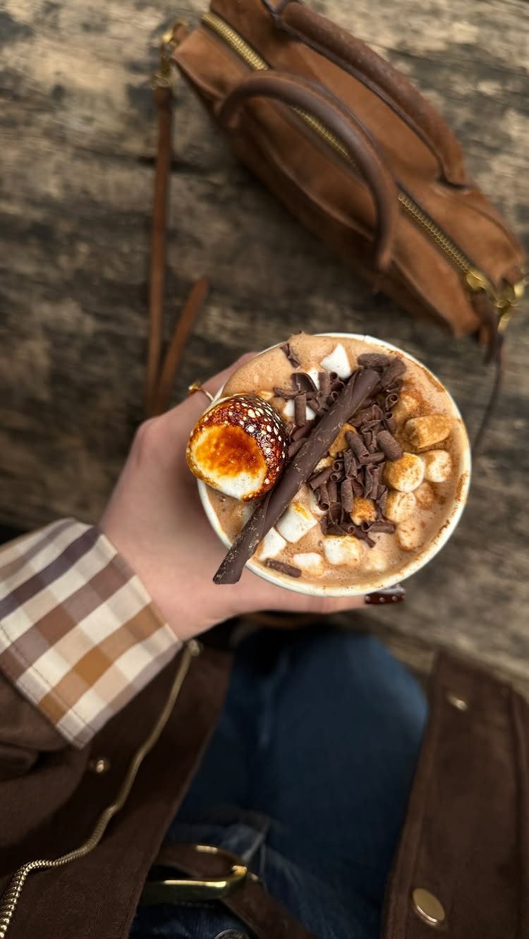 Hot chocolate with toasted marshmallows and chocolate shavings held over a wooden background.
