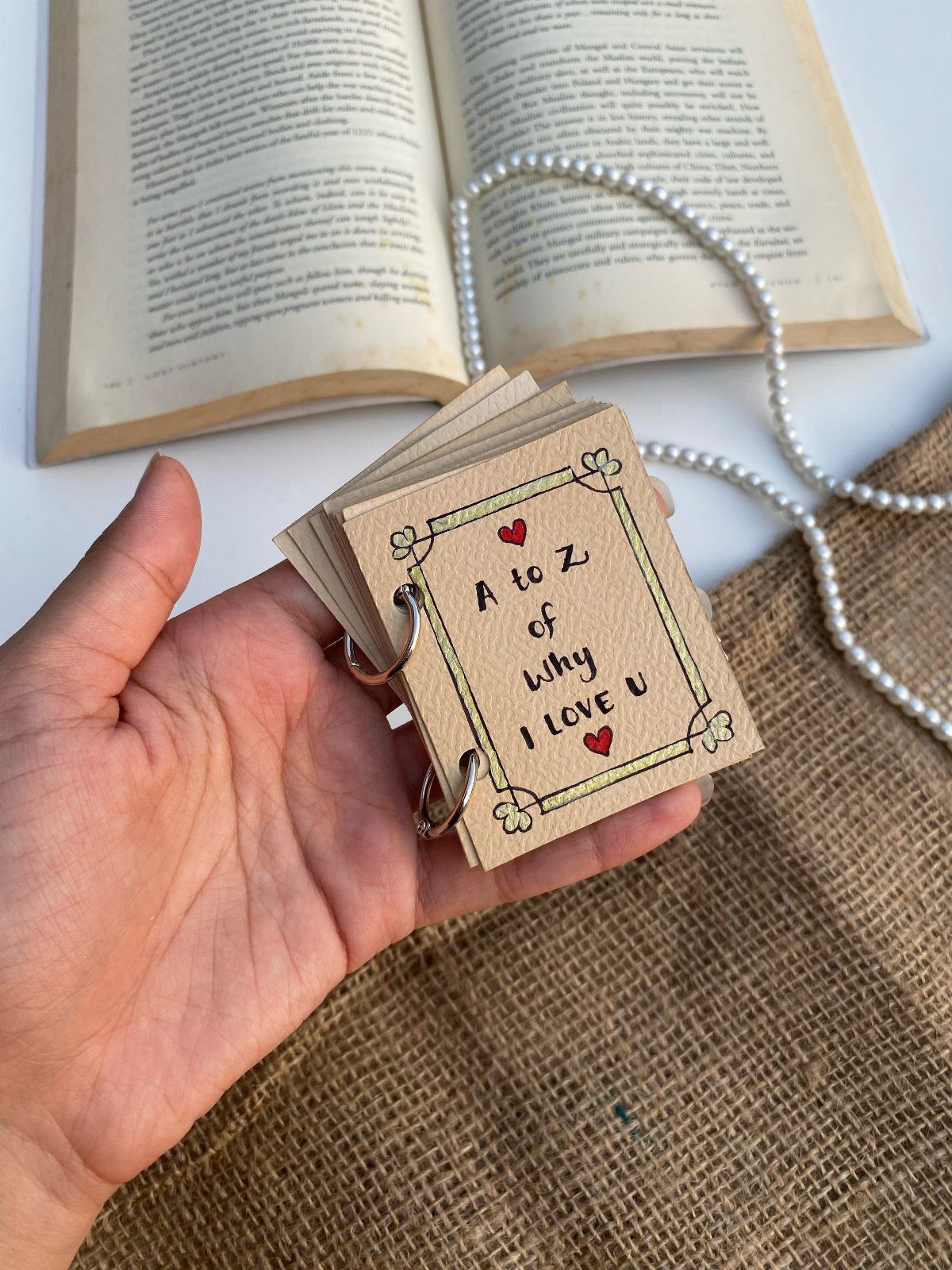 Handmade ring-bound notebook with a love note cover held over an open book.