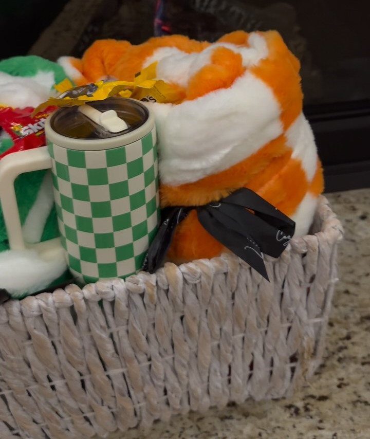 White woven gift basket with a checkered mug and orange plush blanket.