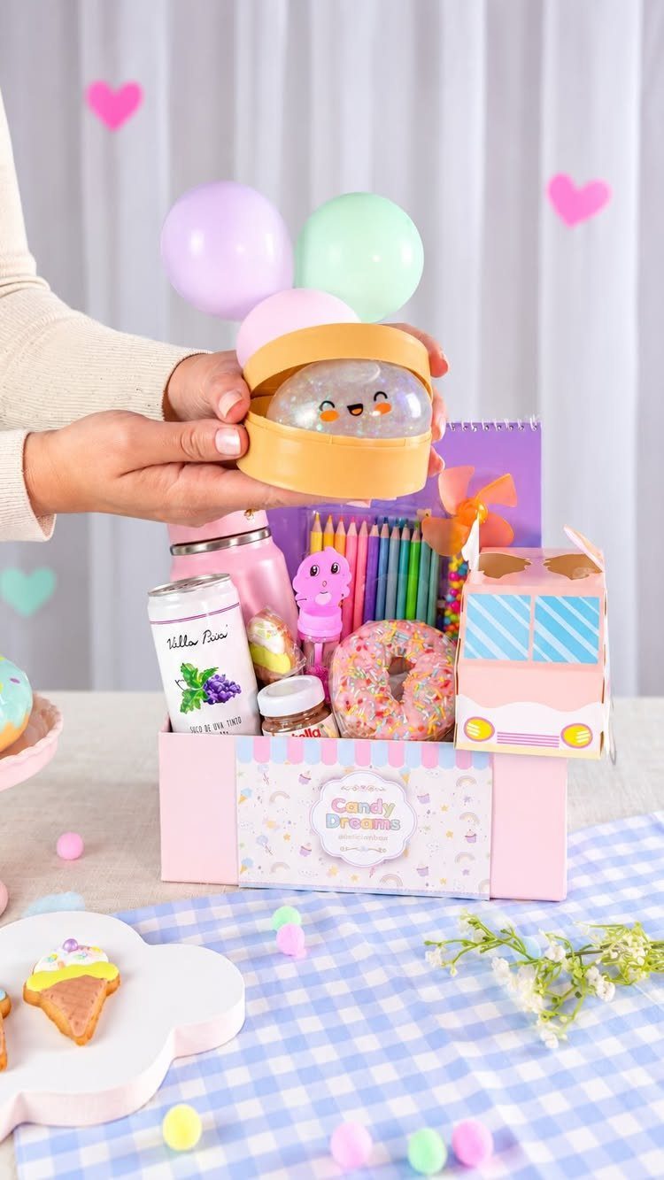 Pink candy box filled with treats and colorful pencils on blue checkered tablecloth