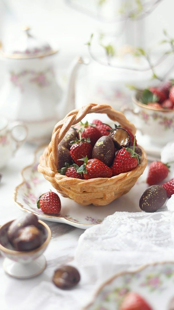 Edible pastry basket filled with fresh strawberries and chocolate treats on floral china