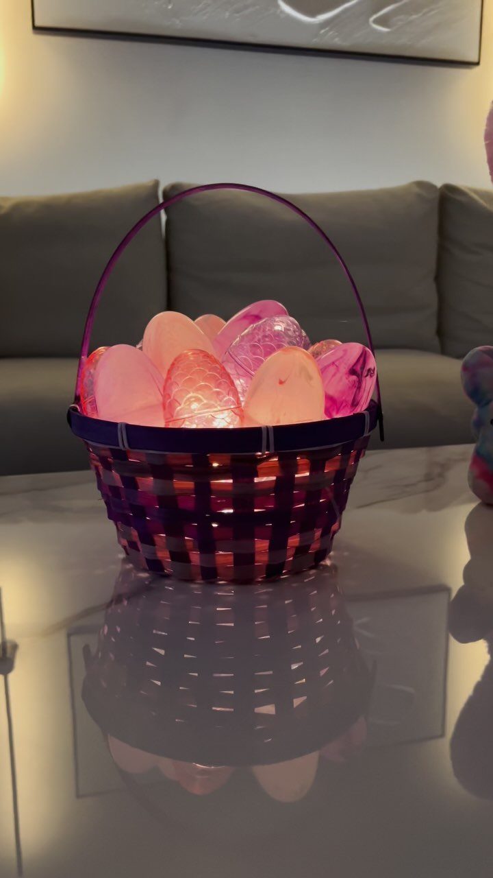 Purple woven Easter basket filled with glowing pink and orange eggs on white table