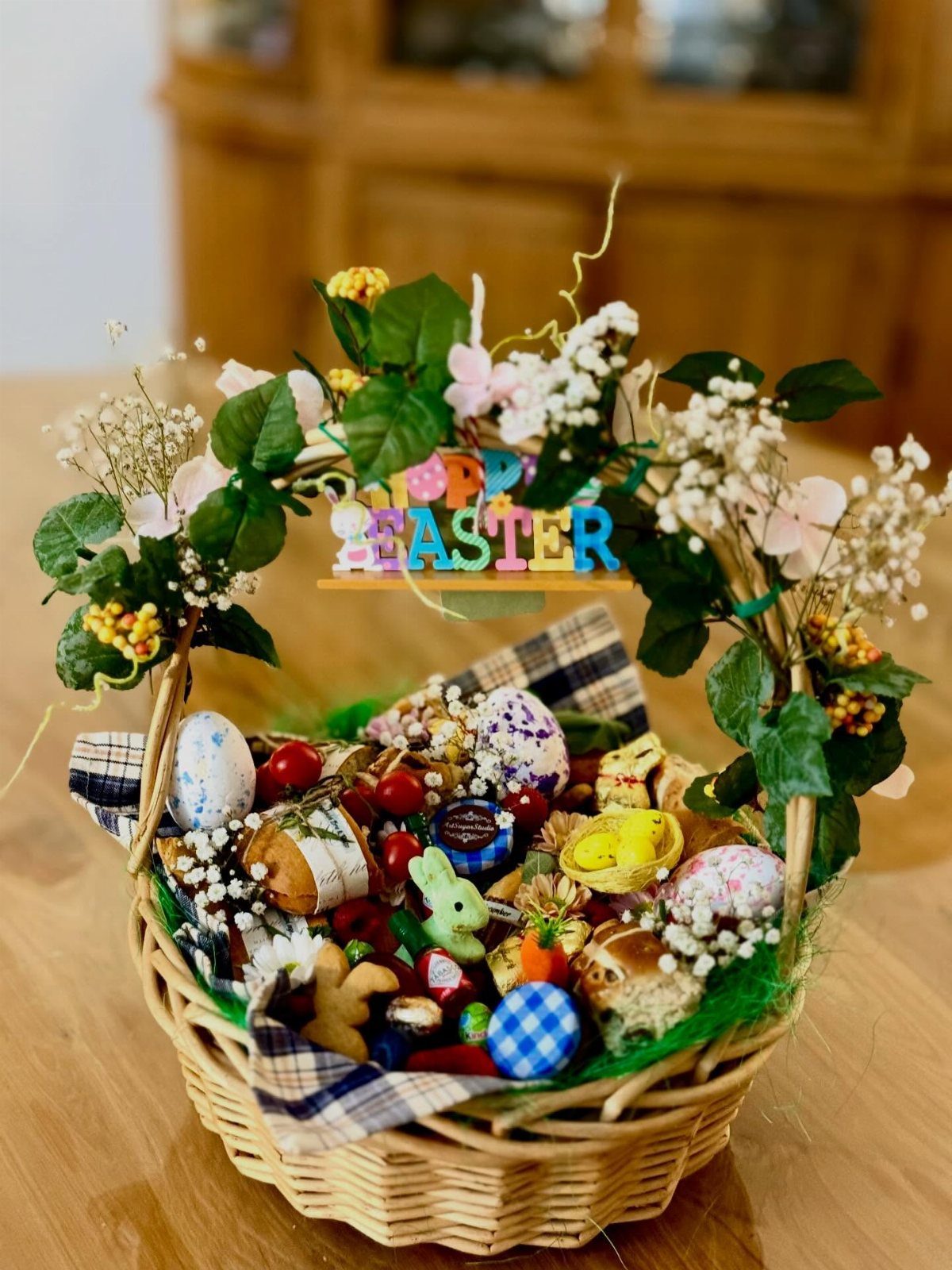 Woven Easter basket filled with treats and eggs, decorated with spring flowers.