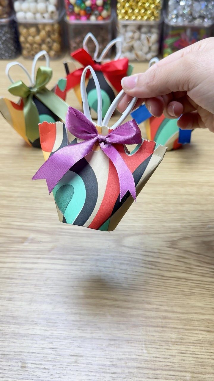 Colorful paper gift bags with ribbons and white handles on a wooden table.