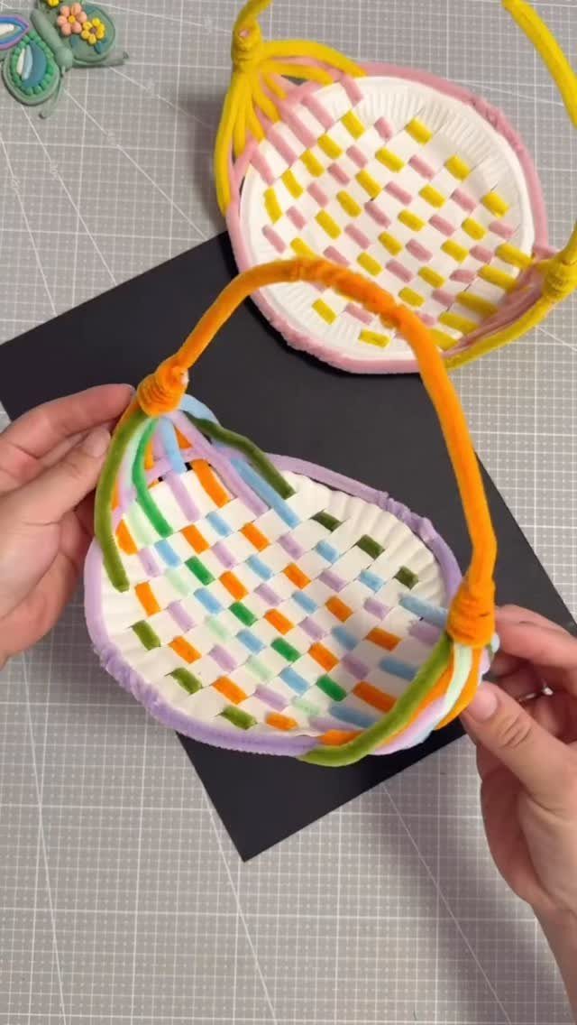 Handmade paper plate baskets woven with colorful pipe cleaners on a grey mat.