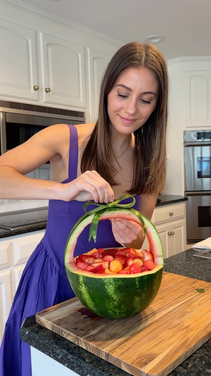 Woman tying a green ribbon on a watermelon carved into a fruit basket.