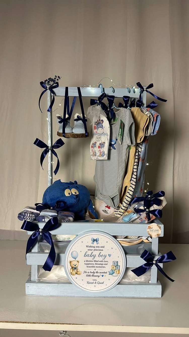 Baby gift basket in a blue wooden crate with clothes and plush toy.
