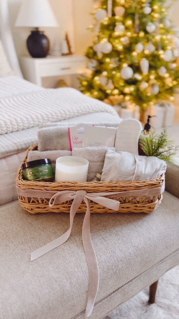 Wicker spa gift basket with towels, candle, and slippers near a Christmas tree.