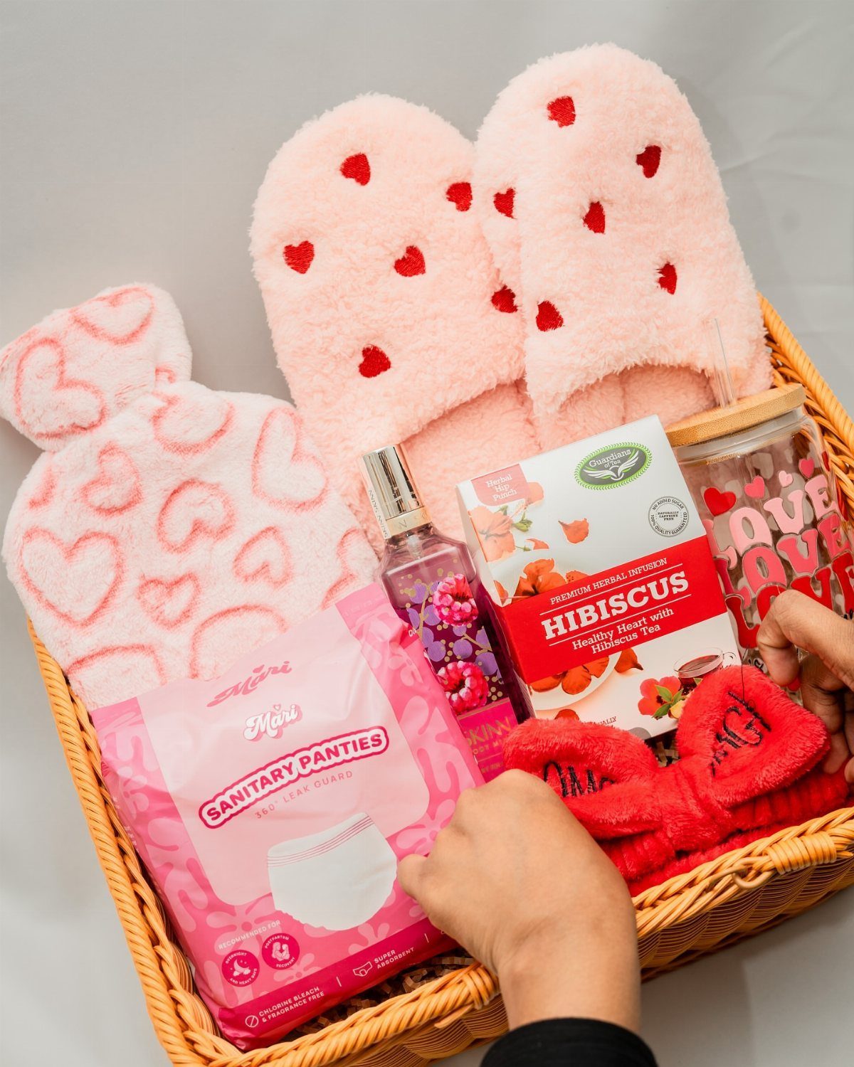Wicker gift basket filled with pink slippers, hibiscus tea, and postpartum recovery items.