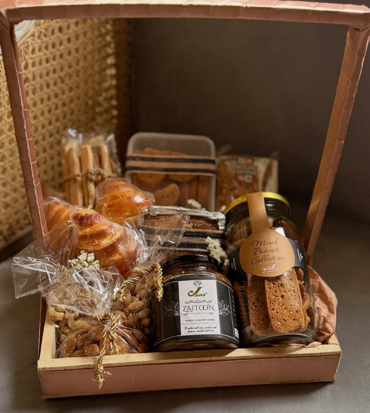 Wooden gift basket filled with croissants, biscuits, nuts, and assorted baked goods.