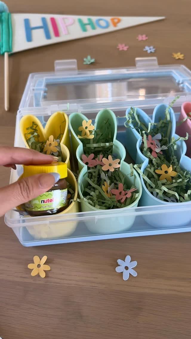 Bunny-shaped plastic bowl baskets filled with green grass and colorful paper flowers.