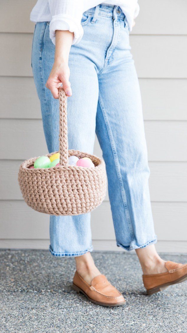 Beige crochet yarn basket filled with pastel Easter eggs held by a person.