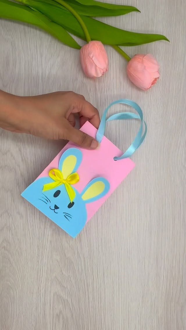 Pink paper gift bag with a blue bunny face and yellow bow handle.