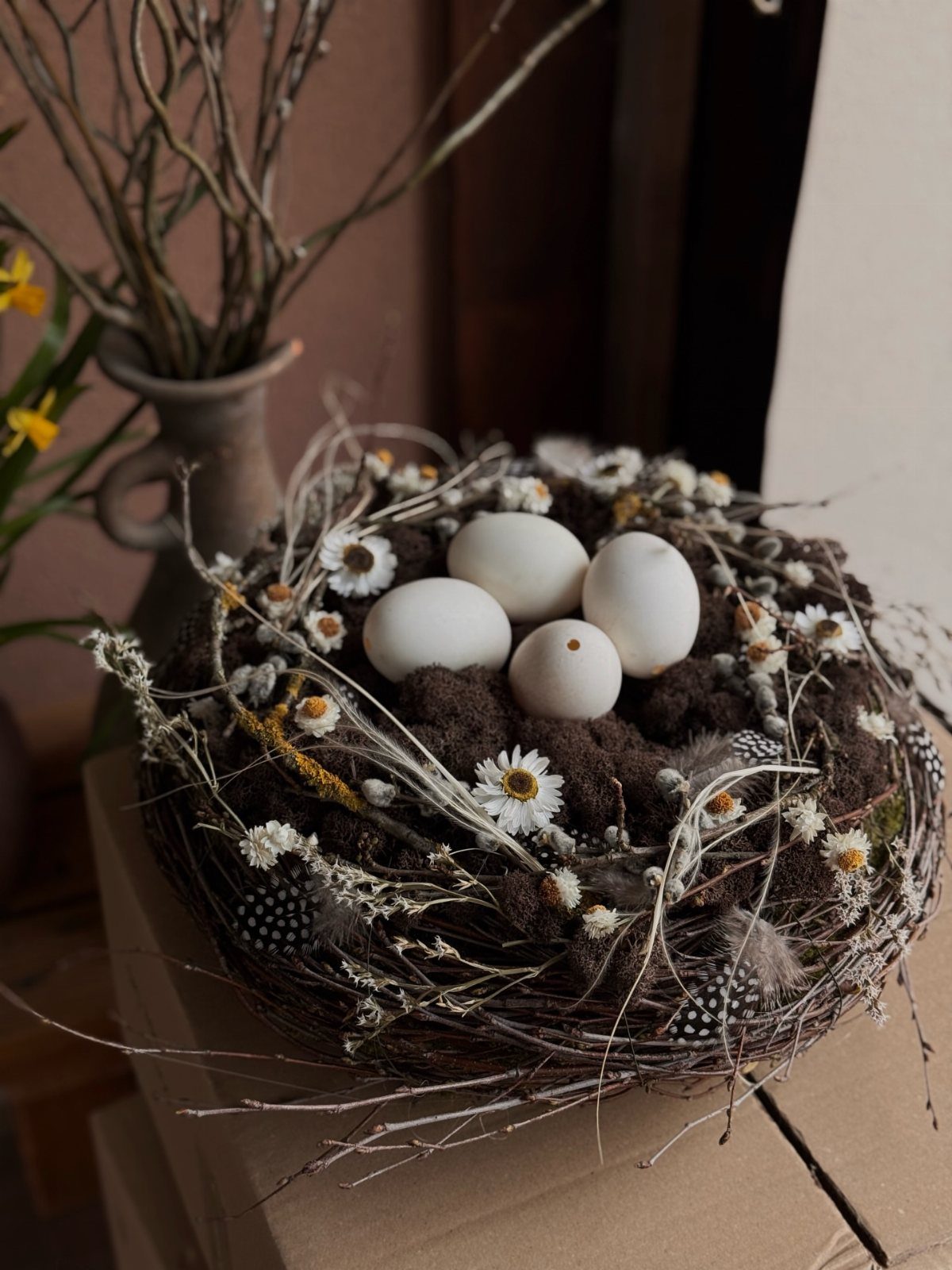 Rustic grapevine and moss nest containing four white eggs and small white flowers.