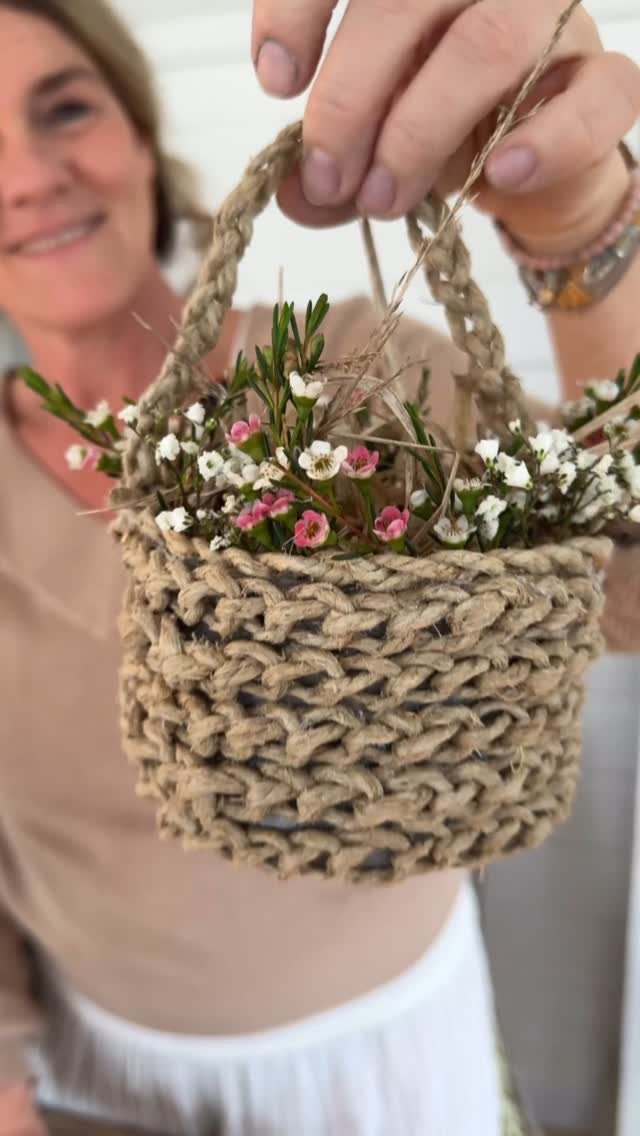 Handmade twine basket filled with small pink and white flowers held by a person